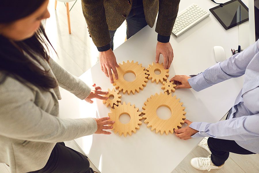 About Our Agency - Group of Employees Holding Wooden Gear Pieces at Office