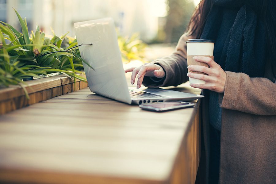 Blog - Woman Typing on Computer While Holding Coffee Outside